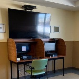 Side by side computers with a privacy divider. A large TV is above both computers